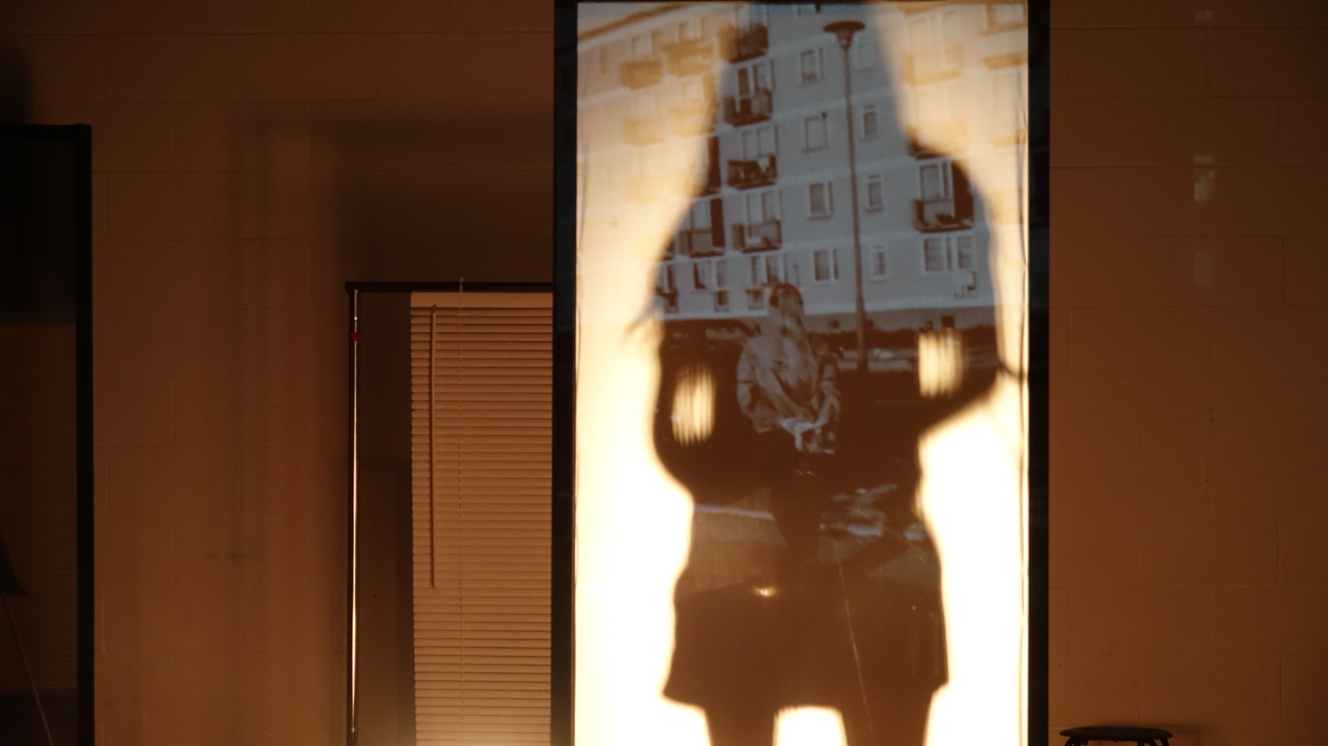performer silhouetted against a black-and-white projection of a woman walking towards an apartment building.